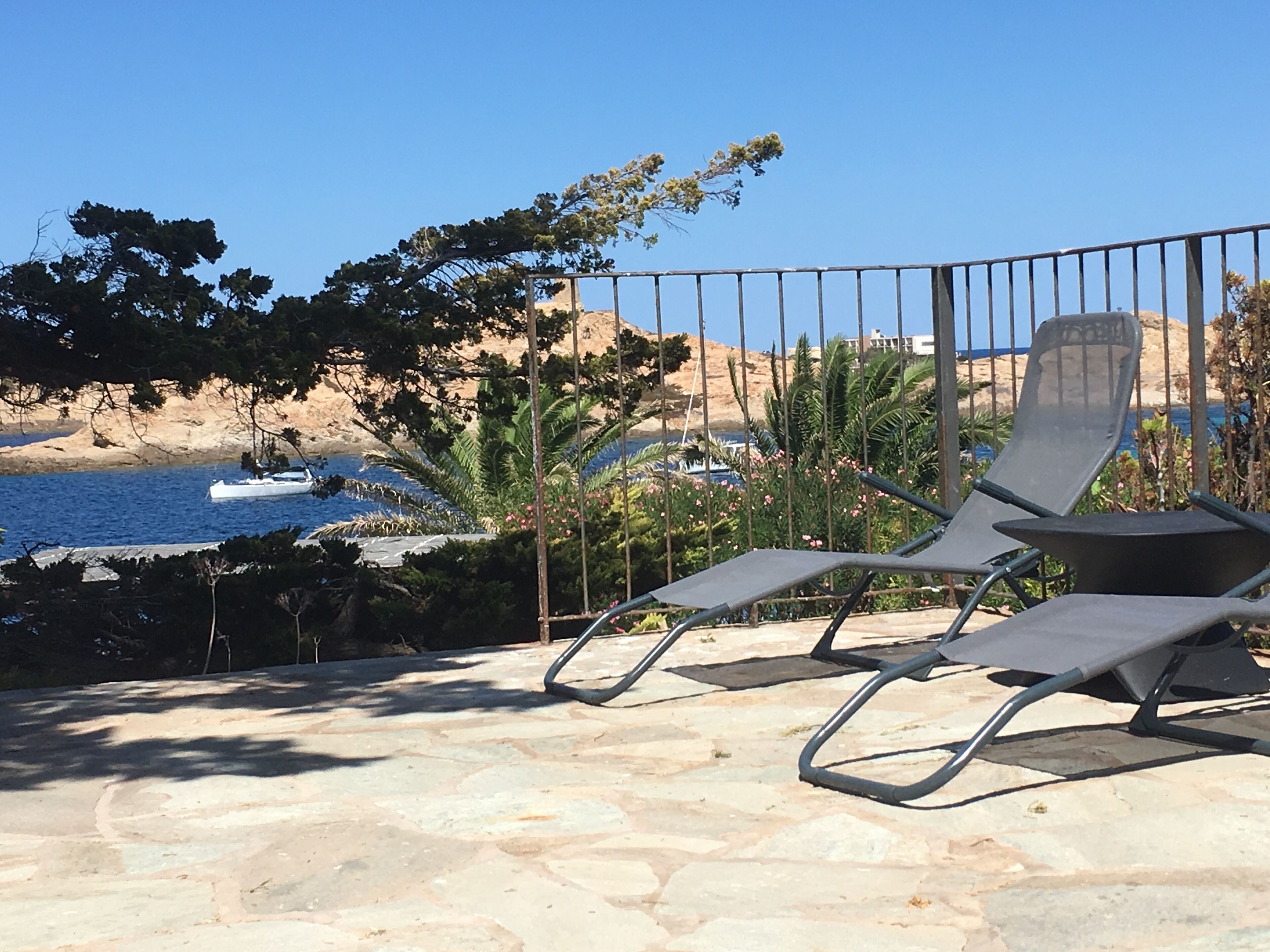 Área da piscina com espreguiçadeiras e vista para o mar e paisagem rochosa.