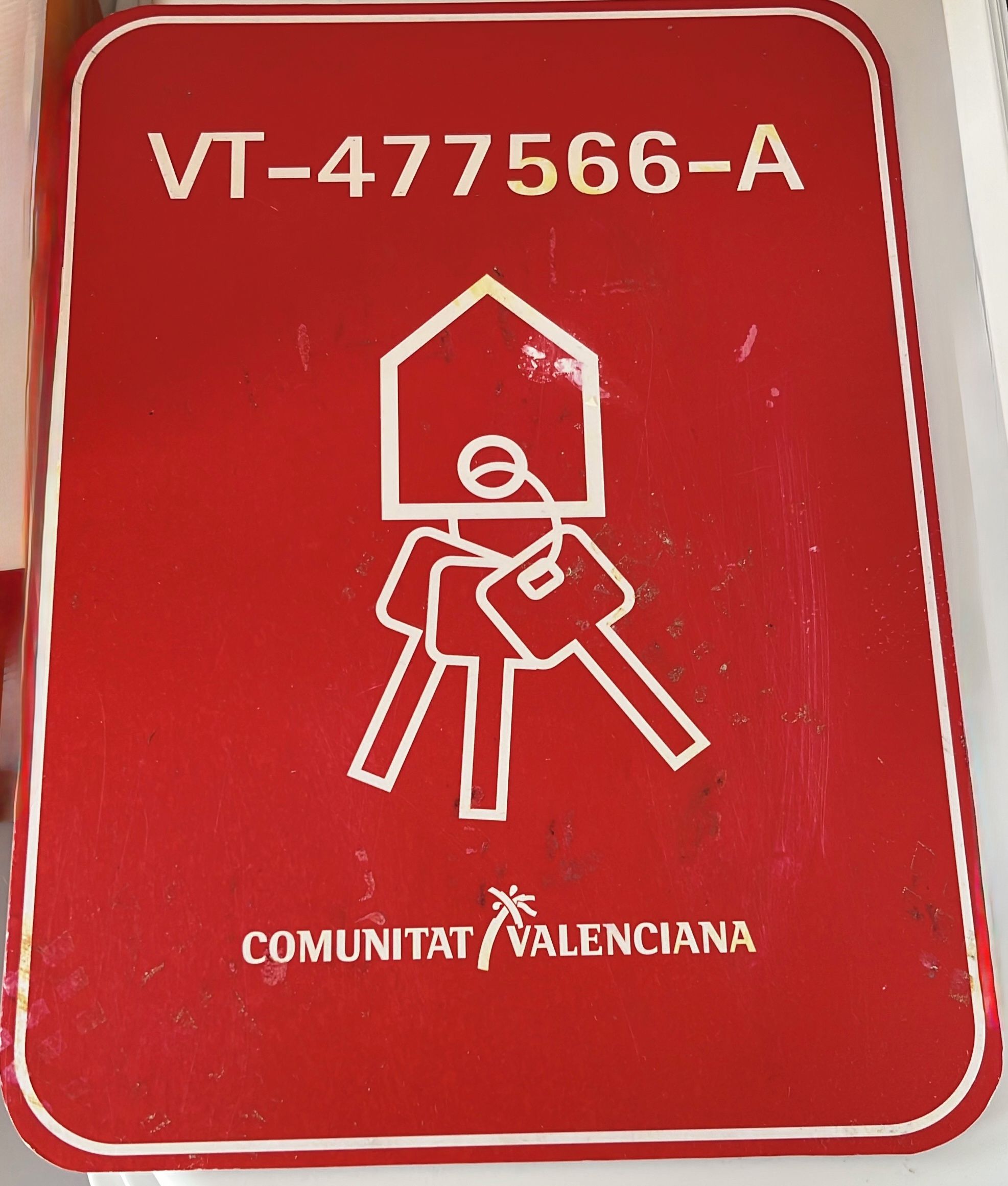 Un panneau rouge avec un pictogramme représentant une maison et les inscriptions « VT-477566-A » et « COMUNITAT VALENCIANA », indiquant un lieu.
