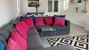 En moderne stue med en grå hjørnesofa, en sort-hvid stribe-rug og et maleri af en båd på væggen.