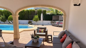 En udendørs patio med pool, siddepladser og plantekasser.