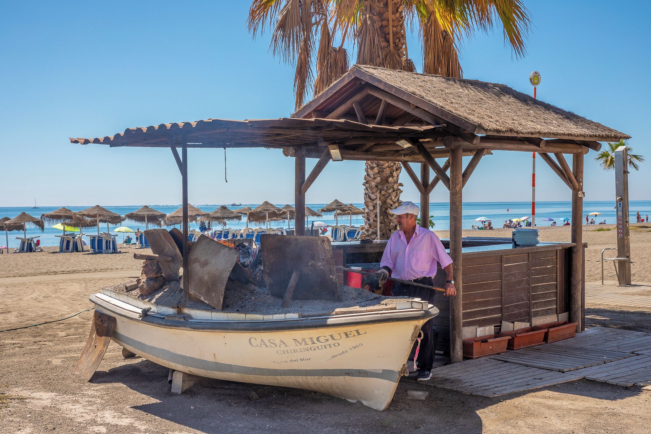 Une scène de plage avec un bateau appelé « Casa Miguel » et une structure en bois.