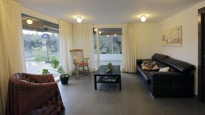 Ein Wohnzimmer mit einem schwarzen Ledersofa, einem Holzschaukelstuhl, einem Tisch mit Muster und einer Topfpflanze.