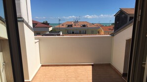 Een balkon met betegelde vloer en uitzicht op omliggende gebouwen en de zee.