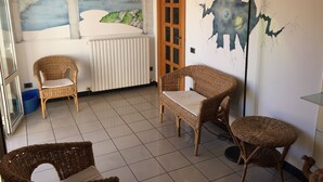 Een kamer met twee rieten stoelen, een klein rond tafeltje, een radiator en een muurschildering van een landschap.