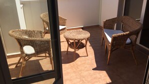 Een balkon met rieten meubels, waaronder stoelen en een kleine tafel, met uitzicht op gebouwen op de achtergrond.
