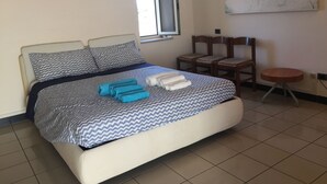 Een netjes opgemaakt bed met beddengoed met een patroon, een klein rond tafeltje en een schilderij aan de muur.