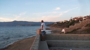 Un hombre de pie sobre una repisa de concreto mirando una playa con casas al fondo.