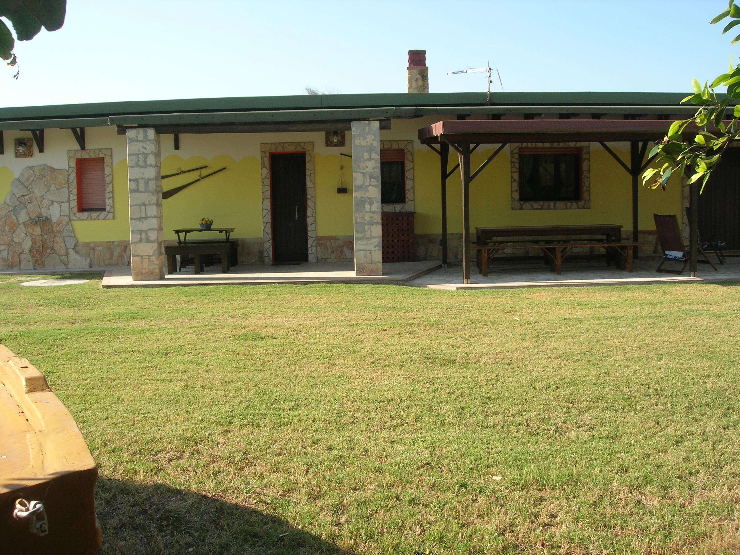 A building with a stone facade, a green roof, and a covered patio area with a bench and table.