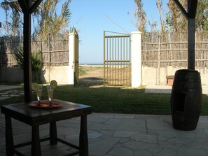 Une terrasse avec une table, un grand bac à fleurs et une vue sur la plage, accessible par un portail.