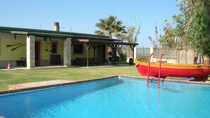 Una piscina con un bote rojo, un porche cubierto y un edificio con techo verde.