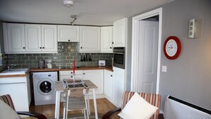 Eine kompakte Küche mit weißen Schränken, einer Waschmaschine, einem Toaster und einem Essbereich mit gestreiften Stühlen und einem Tisch.