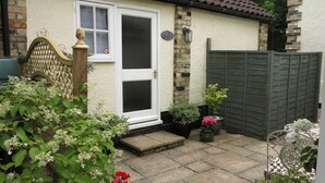 Ein Haus mit weißer Tür, einem Holztor und einem kleinen Garten mit verschiedenen Pflanzen und Blumen.