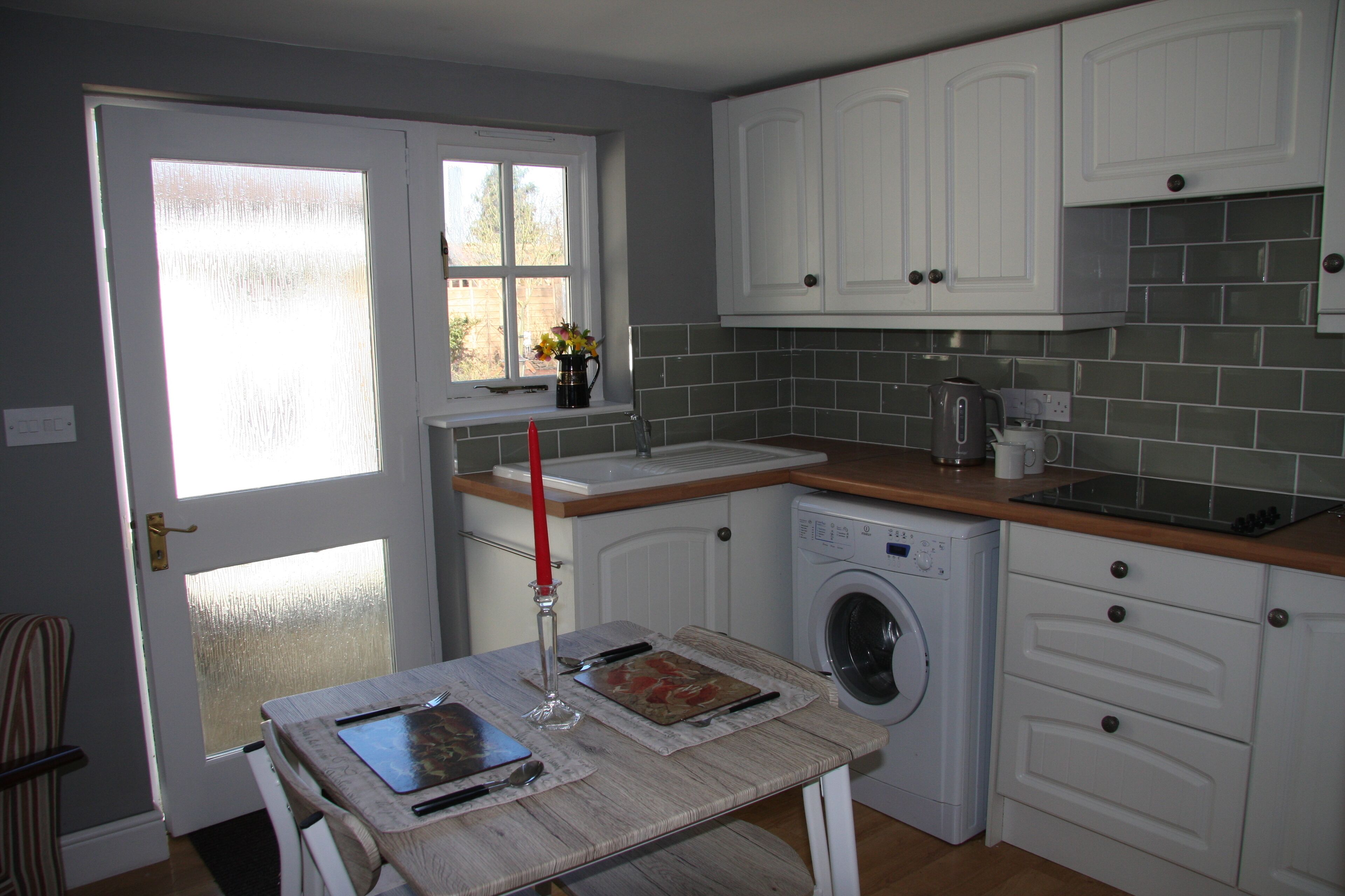 A compact kitchen with white cabinets, a washing machine, and a window with a view.