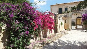 Een traditioneel gebouw met een stenen muur en een poort, omringd door weelderige begroeiing en levendige paarse bougainvillea bloemen.