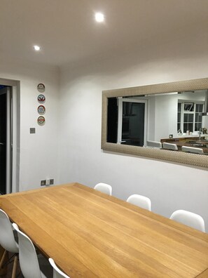 Zona pranzo con tavolo in legno e sedie bianche, uno specchio con cornice lavorata e un muro decorato con quattro elementi circolari.