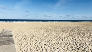 Ein weiter Sandstrand mit Fußabdrücken, einem klaren blauen Himmel und dem Meer im Hintergrund.