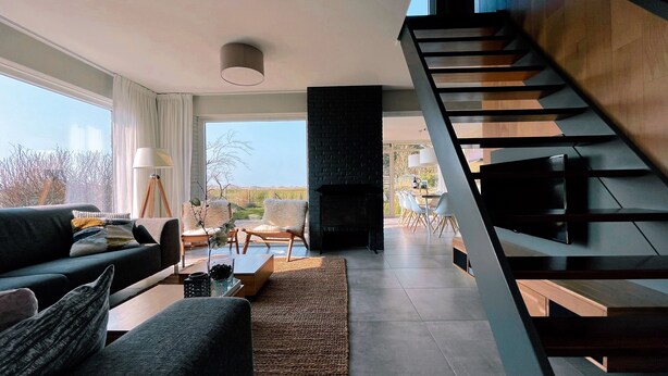 Ein modernes Wohnzimmer mit einer Couch, einem Couchtisch und einem Kamin. Eine Treppe führt zu einem Außenbereich mit Esstisch und Stühlen.