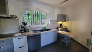 Uma cozinha moderna com máquina de lavar louça embutida, janela com vista para o verde e uma pequena área de jantar com mesa e cadeiras.