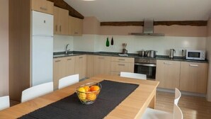 A modern kitchen with wooden cabinets, a built-in oven, a microwave, and a dining area with a table and chairs. - Casa Rural Aranaratxe for 8 people (Aranarache)