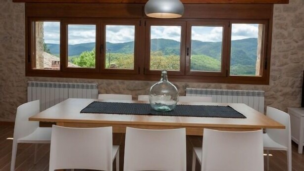 A dining area with a wooden table, white chairs, and a view of mountains through large windows. - Casa Rural Aranaratxe for 8 people (Aranarache)