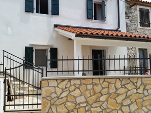 Stunning Mediterranean-style building with a red-tiled roof and stone wall, featuring a black metal gate and multiple windows with black shutters.