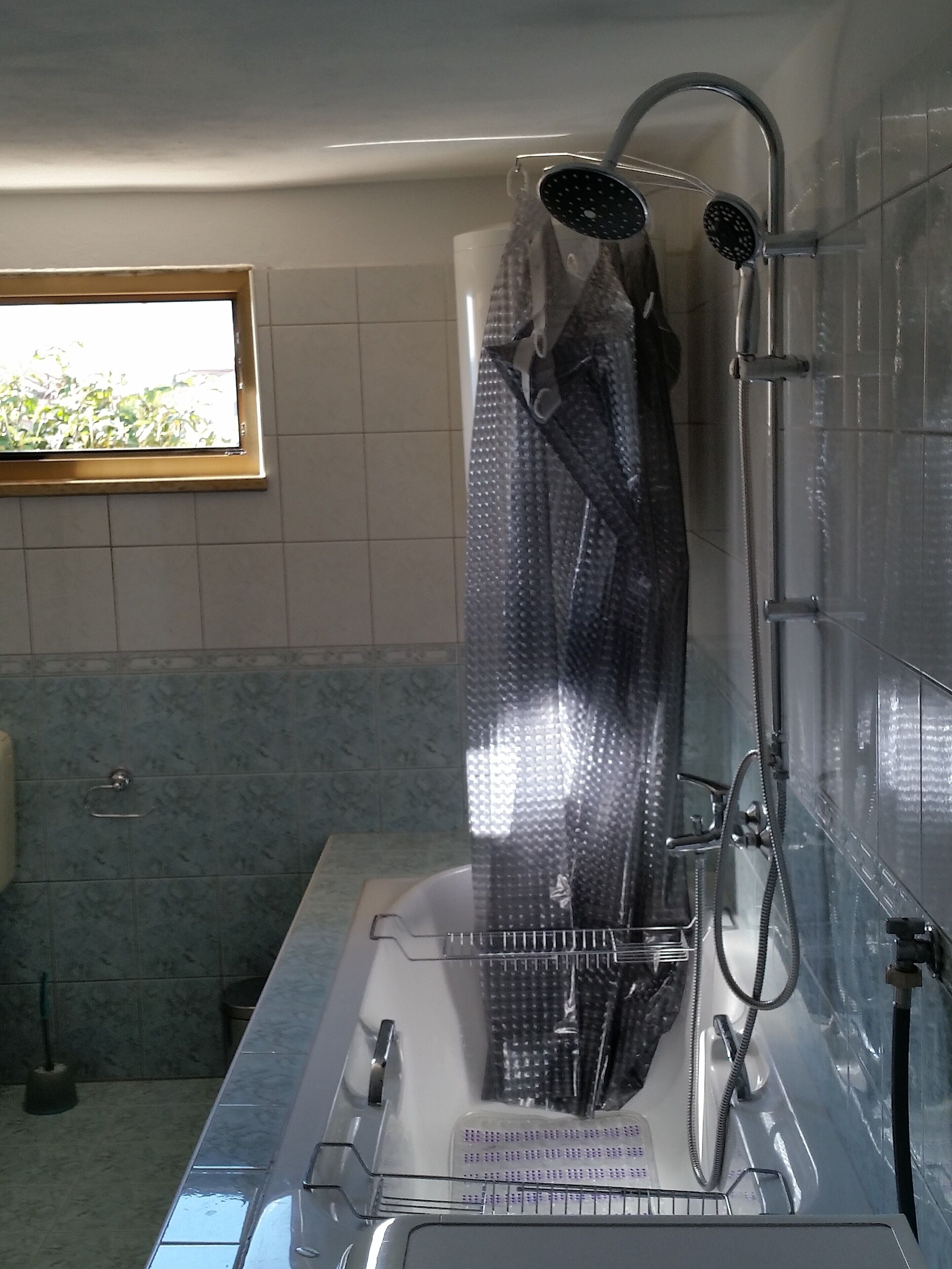 A bathroom with a shower, a window, and a tiled floor.