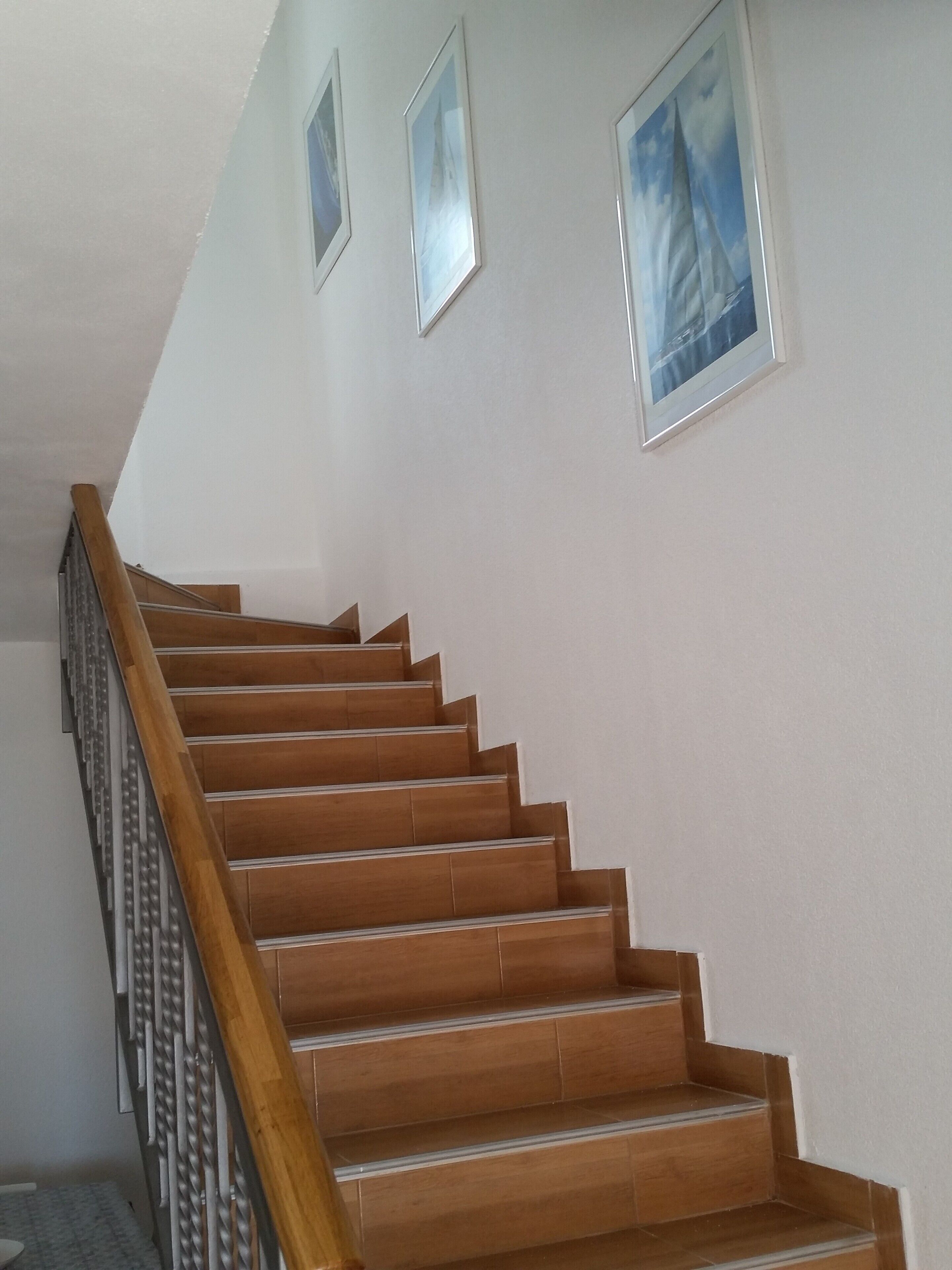 Una escalera de madera con baranda de metal, paredes blancas y cuadros enmarcados.