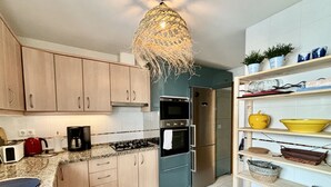 Une cuisine moderne avec des meubles en bois, un réfrigérateur en acier inoxydable, une cuisinière à gaz et un luminaire suspendu.