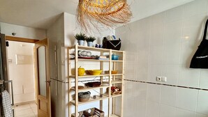 Une pièce avec un sol carrelé de carreaux blancs, une étagère en bois contenant divers objets, un lustre en osier et un sac noir accroché au mur.