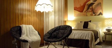 A bedroom with a bed, two chairs, a lamp, and a painting on the wall.