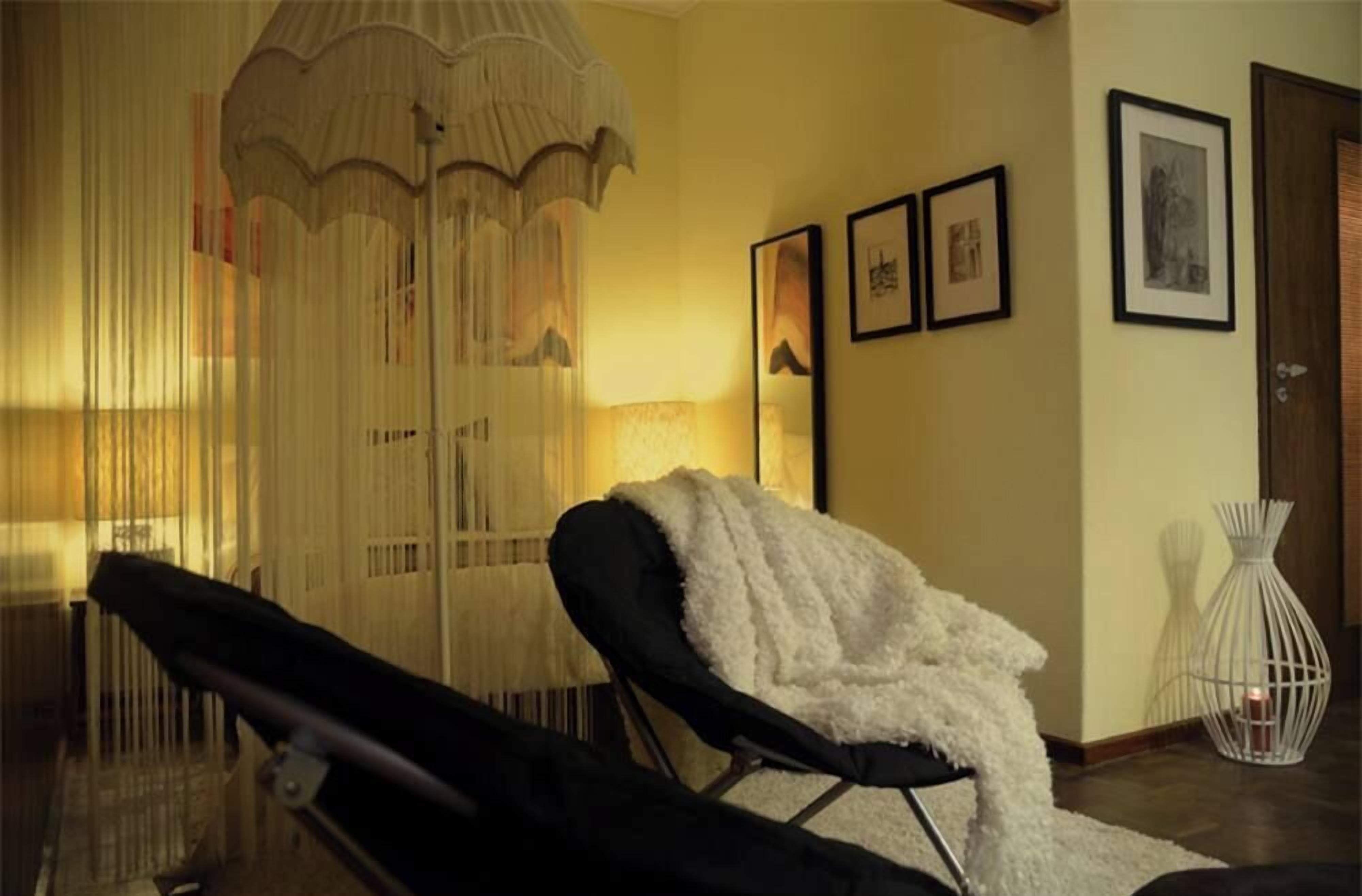 A room with a black lounge chair, a white fluffy throw, a hanging light fixture, and framed pictures on the wall.