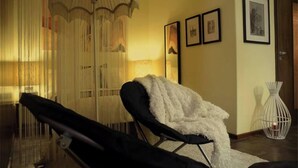 Une pièce comprenant un fauteuil de couleur noire, un plaid blanc et moelleux, un luminaire suspendu et des tableaux encadrés accrochés au mur.