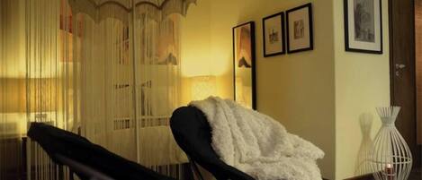 A room with a black lounge chair, a white fluffy throw, a hanging light fixture, and framed pictures on the wall.