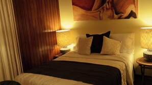 Une chambre d’hôtel avec un lit, deux lampes de chevet, un tableau au mur et un rideau.