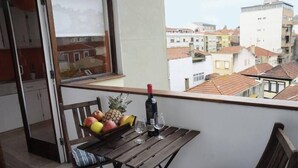 Un balcon avec une table en bois, un panier de fruits et une bouteille de vin.