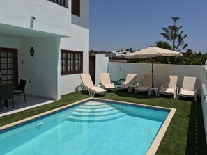 Area piscina con una vasca rettangolare, circondata da erba sintetica e dotata di numerosi lettini.