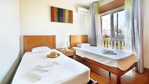 Hotellihuone, jossa on kaksi erillistä sänkyä, puinen pääty, yöpöytä lampun kanssa ja ikkuna, jossa on verhot.