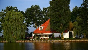 A house with a red roof, a small balcony, and a pond in front. - Unique farmhouse right on the water in a beautiful location (Warten)