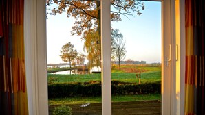 A view through a sliding glass door to a garden with a pond, trees, and a grassy area. - Unique farmhouse right on the water in a beautiful location (Warten)