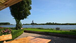 A wooden table and bench by a riverside with a clear view of the water and distant trees. - Unique farmhouse right on the water in a beautiful location (Warten)