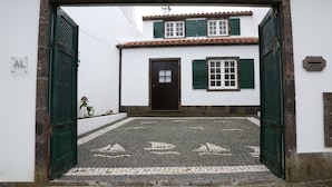 Ein Innenhof mit Kopfsteinpflaster, ein weißes Gebäude mit grünen Fensterläden und einer schwarzen Tür.