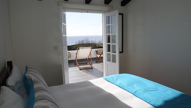 Ein Schlafzimmer mit Bett, Meerblick durch eine offene Tür und einem Balkon mit Stuhl.