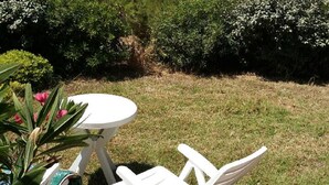 A patio with a round table and two chairs, surrounded by greenery and a view of the sea.