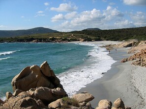 Une plage avec de gros rochers au premier plan, une étendue de sable et un paysage vallonné en arrière-plan.