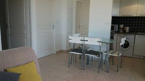 A compact living space with a dining area, a sofa with cushions, a washing machine, and a tiled floor.