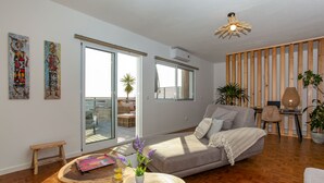 A spacious living room with a large sofa, a wooden coffee table with a book and a plant, and a balcony with a view.