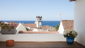 A balcony with a view of the sea, a church tower, and potted plants.
