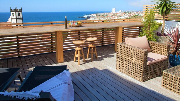 A wooden deck with wicker furniture, a bottle, and glasses on a terrace overlooking the sea.