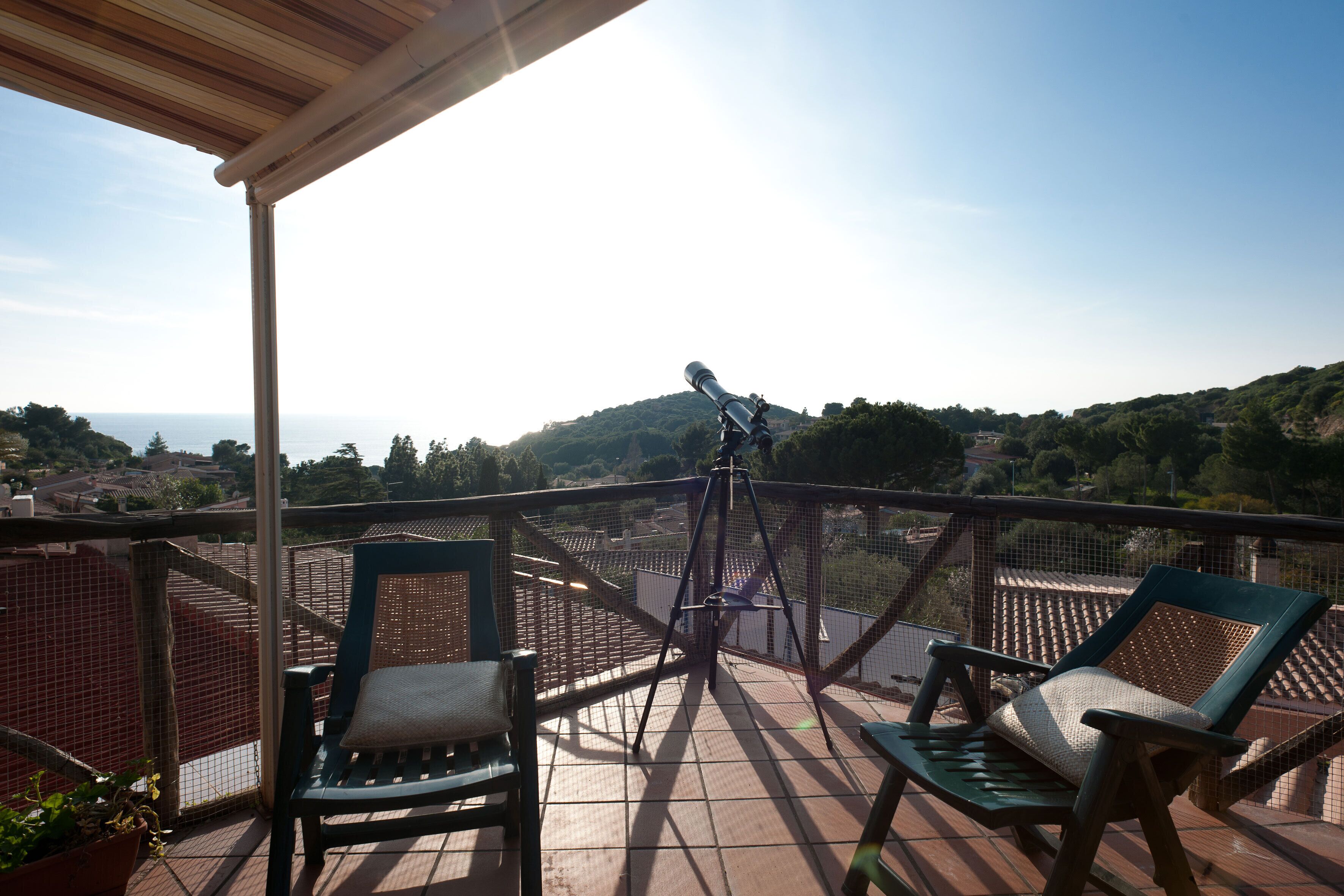 Un balcón con dos sillas, un telescopio y vistas al mar y las colinas.