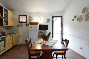 Een kleine keuken met een eethoek, met een houten tafel, stoelen, een koelkast en een televisie.